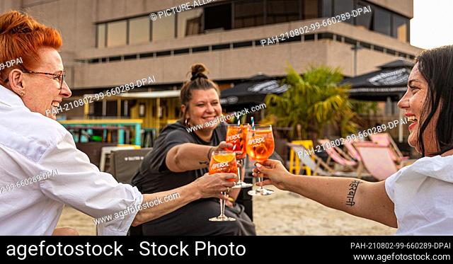 25 July 2021, Lower Saxony, Hanover: The girlfriends, Peggy (l-r), Valerie and Mandy, toast with their mixed drinks in summery weather at the beach bar...