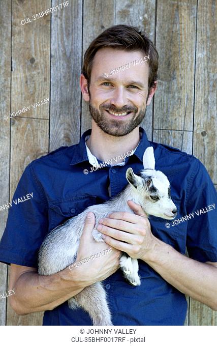 Man holding kid goat outdoors