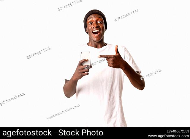 Portrait of young excited african-american guy recommending smartphone app, pointing finger at mobile phone with amazed and happy face