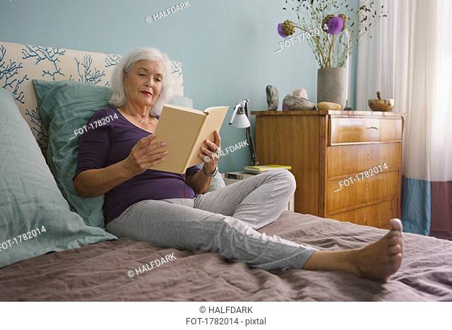 Senior woman reading book on bed