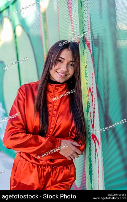 Woman smiling while leaning on graffiti fence