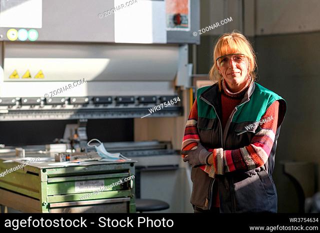portrait of a woman standing in front of a CNC machine in goggles and working in a modern metal production and processing factory. High quality photo