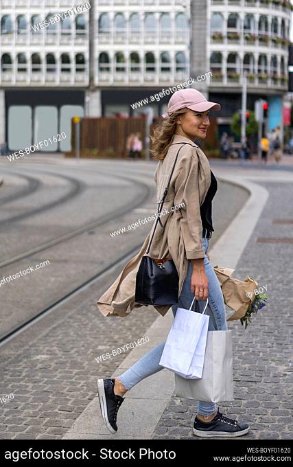 Smiling young woman walking with shopping bags crossing railroad track