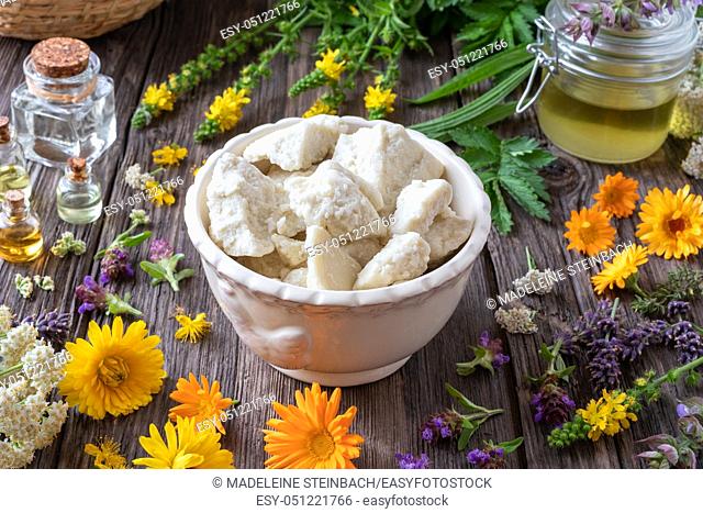 Raw shea butter in a bowl with essential oils and medicinal herbs - ingredients for preparing a homemade skin cream
