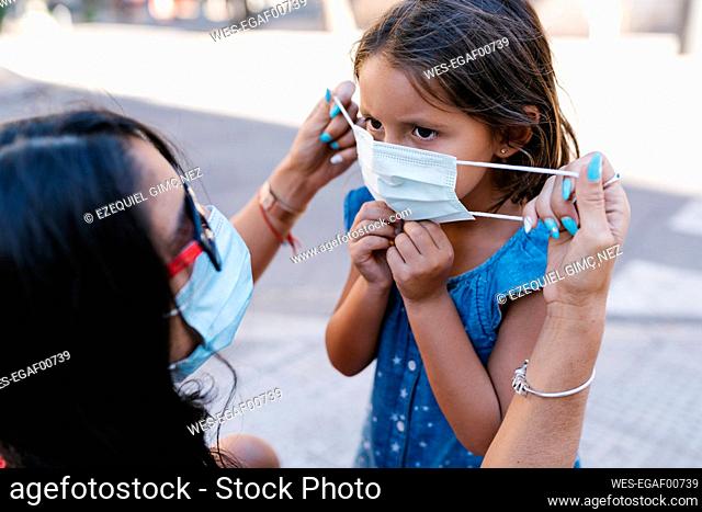 Close-up of mother wearing face mask to daughter on street