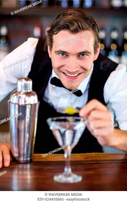 Portrait of bartender garnishing cocktail with olive