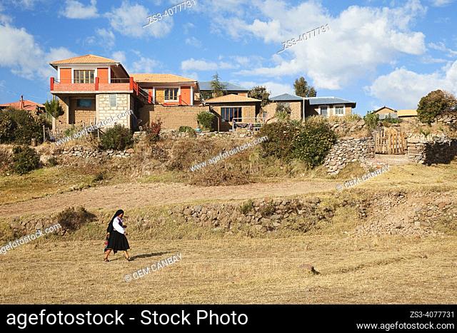 Indigenous woman in traditional dress walkingin front of the traditional houses in Amantani island, Lake Titicaca, Puno Region, Peru, South America