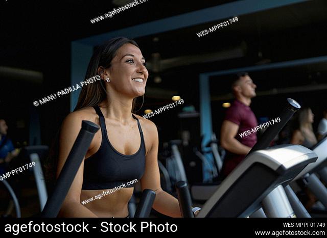 Smiling female athlete looking away while exercising on treadmill at gym