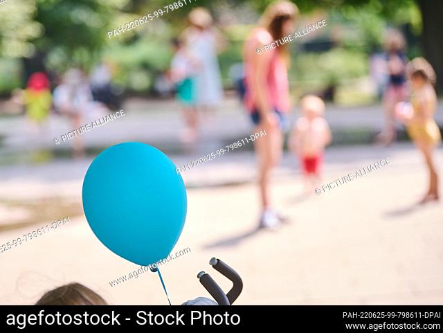 25 June 2022, Berlin: A balloon hangs from a stroller while parents play with their children at the watering hole in Volkspark am Weinberg