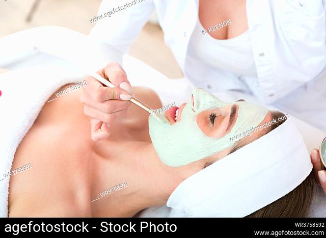 Beautician applying face peeling mask to woman in beauty salon