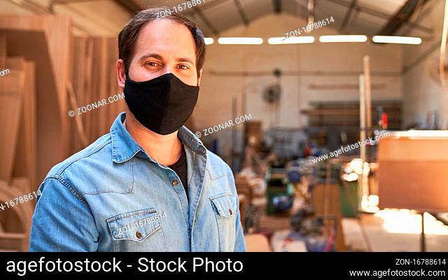 Junger Mann als Handwerker Azubi mit Mundschutz wegen Covid-19 in der Werkstatt