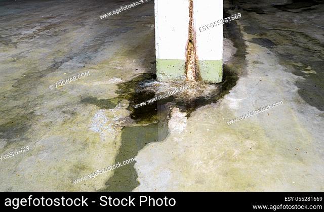 water damage in concrete construction with calcium and rust deposits and puddles near a supporting wall pillar in a garage