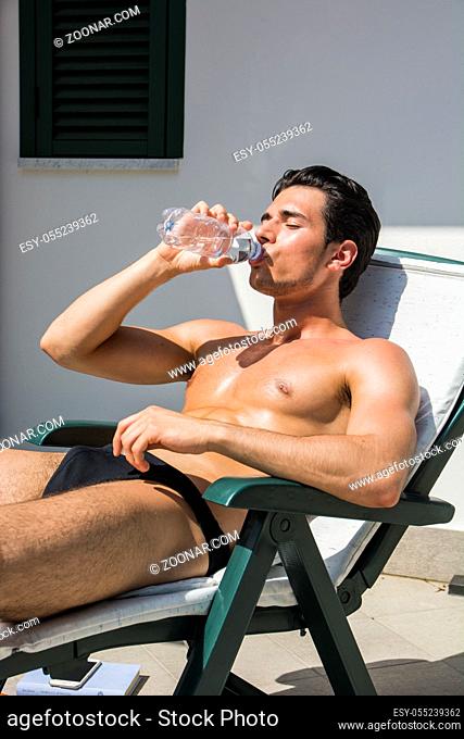 Shirtless Young Man Drying Off in Hot Sun, Drinking Water from Plastic Bottle, Muscular Man Wearing Bathing Suit Sunbathing on Beach Lounge Chair