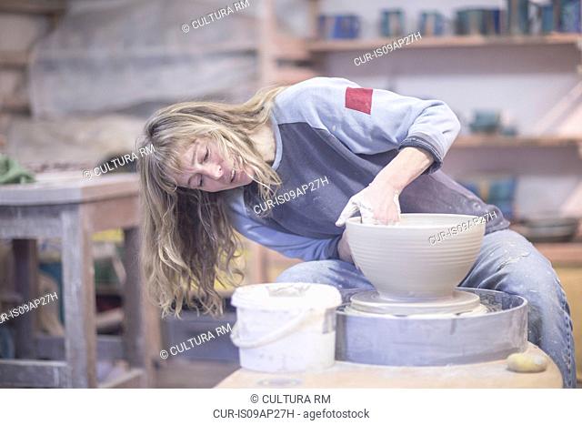 Female potter shaping clay bowl on pottery wheel in workshop