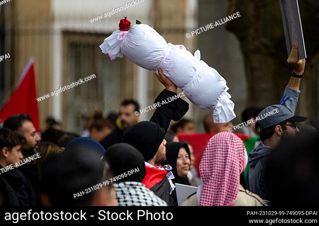 29 October 2023, Baden-Württemberg, Stuttgart: During a pro-Palestine rally in Schlossplatz, a man lifts up a wrapped bundle of cloth meant to symbolize a dead...