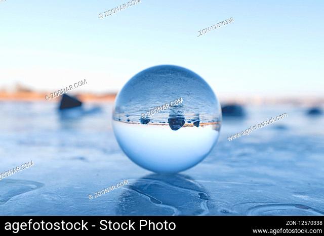 Crystal ball on a frozen lake in the winter with black rocks in the background