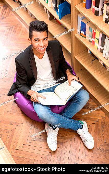 Top view of handsome man sitting on the floor near bookshelves and reading books in library