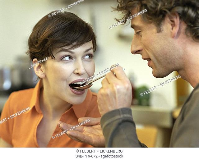 Mid adult man with curly hair feeds his girlfriend with a spoon, close-up