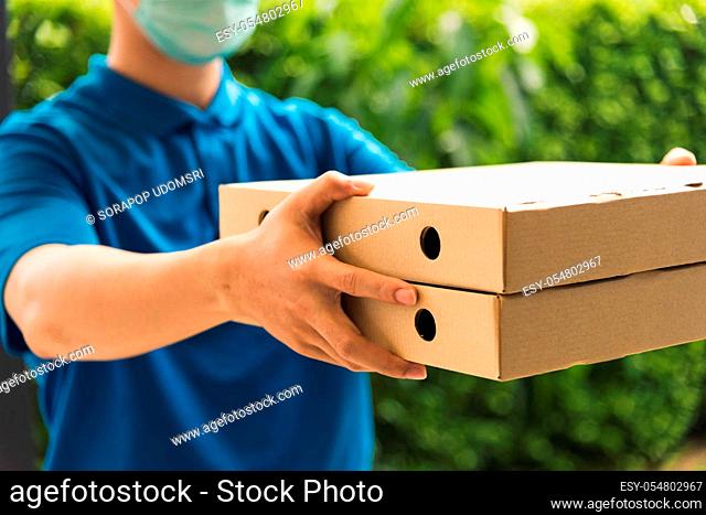 Asian young delivery man courier sending and holding fast food pizza boxed in uniform he protective face mask service customer at home door