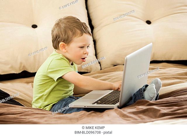 Caucasian boy using laptop on bed