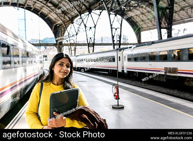 Mid adult woman with laptop bag looking away while standing on railroad station platform