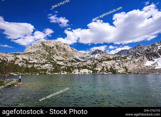Hiker on the shore of Treasure Lake under the Sierra Crest, John Muir Wilderness, Sierra Nevada Mountains, California USA