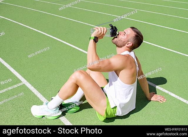 Athlete drinking water sitting on sports field