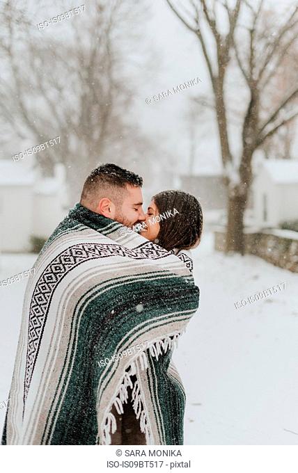 Couple wrapped in blanket kissing in snowy landscape, Georgetown, Canada