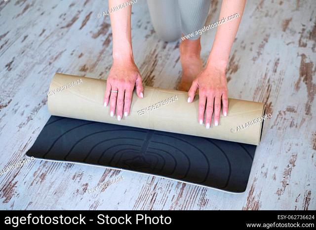 Woman hands roll up yoga mat after class in studio. The concept of a healthy lifestyle