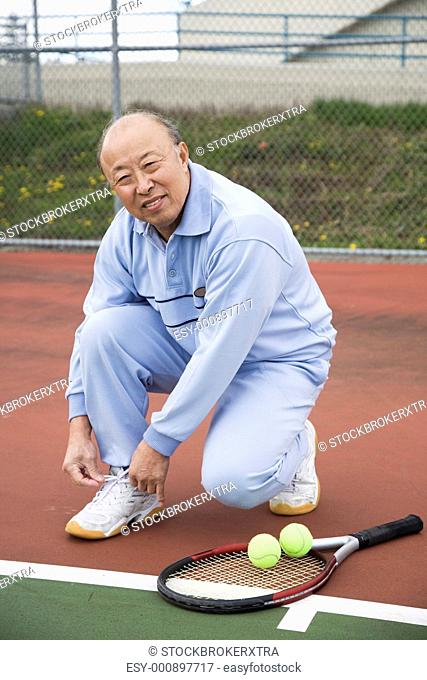 A shot of a senior asian tennis player tying up his shoes