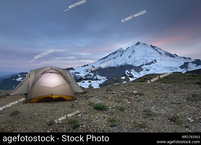 A small tent pitched on a screen slope just below the snowline, at sunset in the Mount Baker wilderness