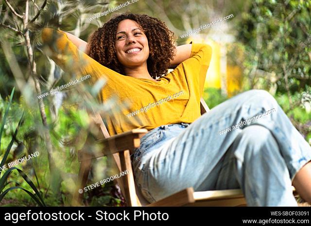 Smiling woman relaxing in garden chair in springtime in sustainable organic vegetable garden