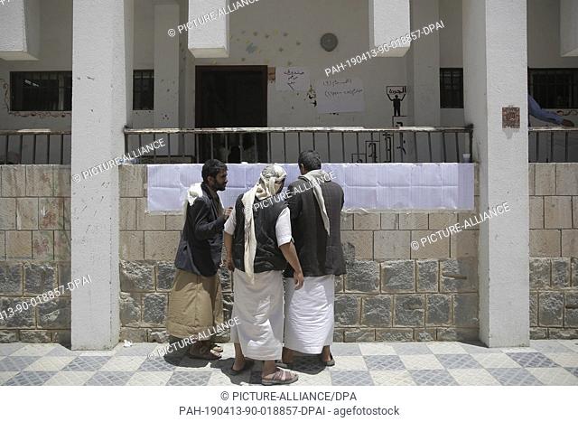 13 April 2019, Yemen, Sanaa: Yemeni men look for their names on the voter lists before casting their votes at a polling station during a complementary...