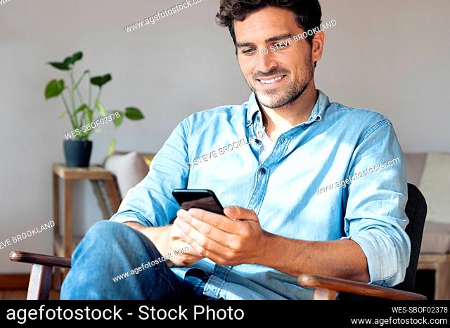 Mid adult man using mobile phone while sitting on armchair at home