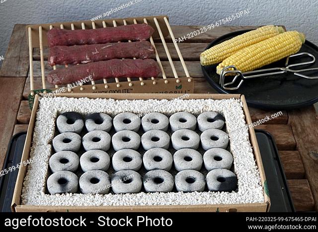 17 July 2021, Berlin: A disposable grill stands on a table after lighting the stones. Next to it is a plate with corn on the cob and tongs