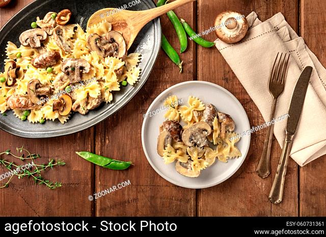 Mushroom and cheese pasta. Farfalle with cremini and green peas, shot from above with ingredients on a dark rustic wooden background