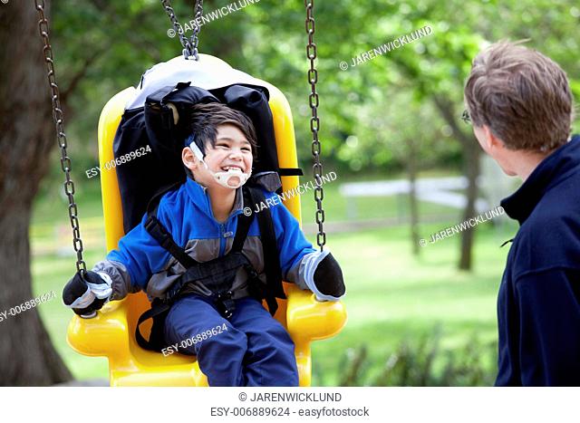 Father pushing disabled son on yellow handicap swing