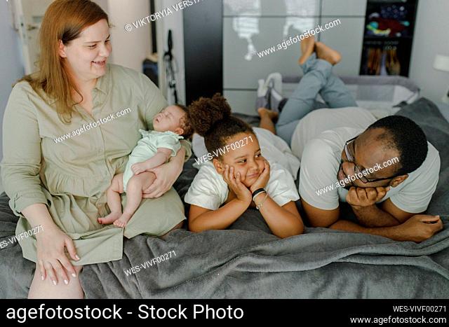Happy mother carrying baby girl with father and daughter lying on bed at home