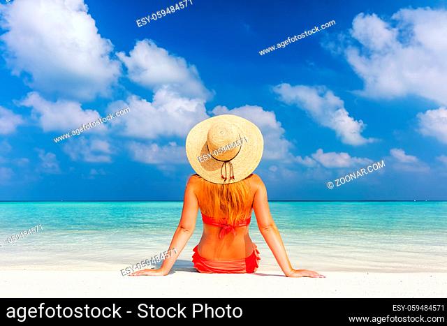 Beautiful young woman in sunhat sitting relaxed on sand, tropical beach in Maldives