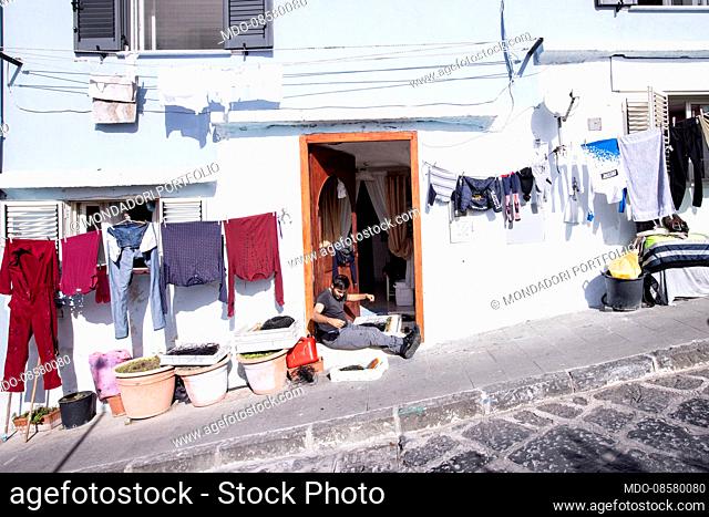 A man works sitting on the front door of the house. Procida (Italy), February 6th 2021