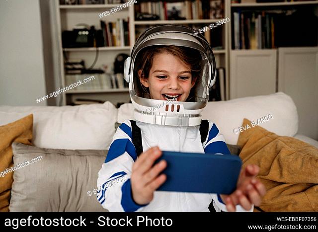 Happy girl wearing space costume having video call on mobile phone at home