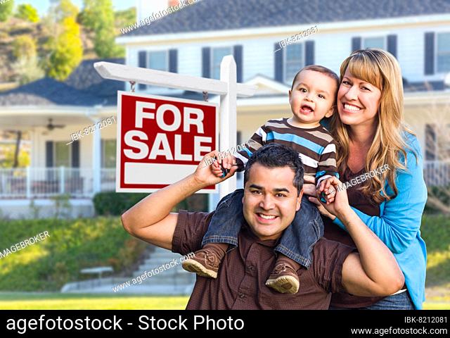 Happy young mixed-race family in front of for sale real estate sign and new house