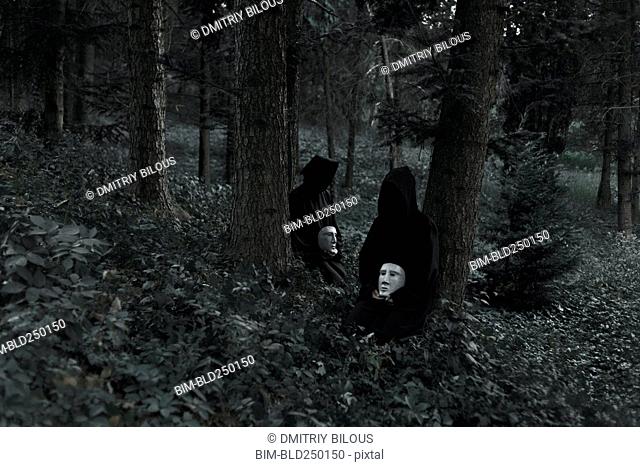 People wearing black robes and holding white masks sitting in forest