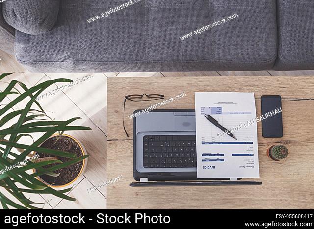 Top view of home office workplace. Laptop, invoice and eyeglasses on wooden table, sofa