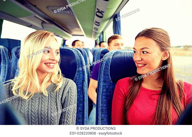 transport, tourism, friendship, road trip and people concept - happy young women sitting and talking in travel bus