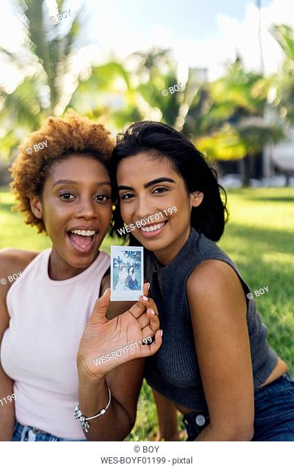 Two happy female friends showing an instant photo in a park
