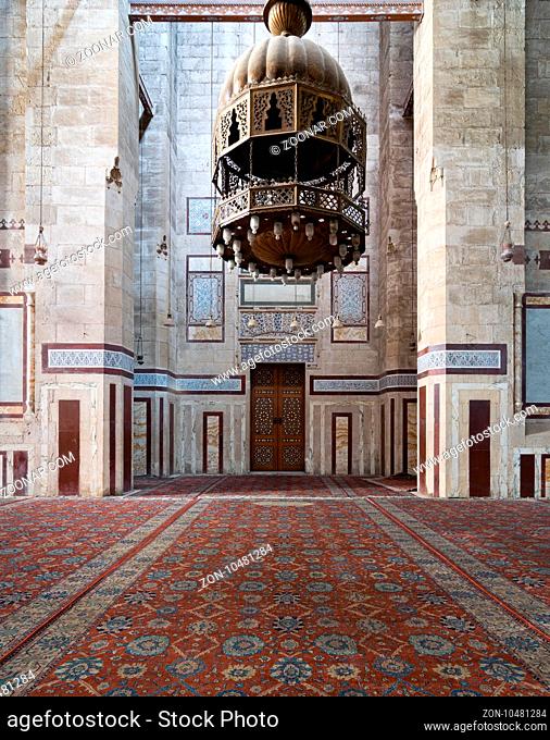 Interior shot of Al Rifaii Mosque (Royal Mosque) with big iron chandelier, decorated marble wall and ornate wooden door, located in front the Cairo Citadel