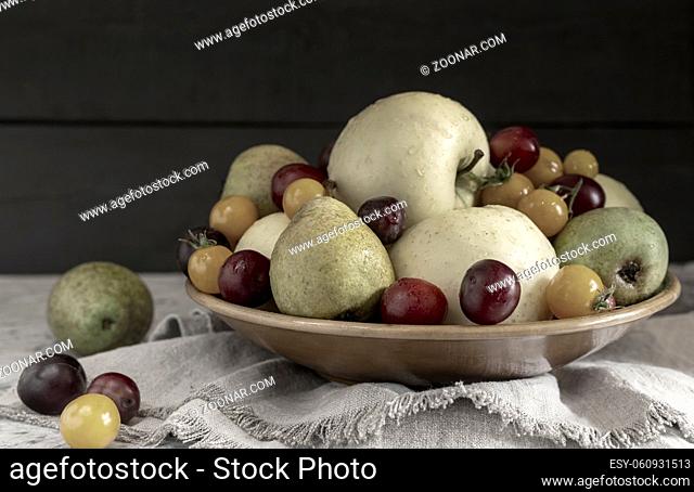 Still life: apples, pears, plums in a ceramic plate. Presented in close-up on a dark background. Front view, copy space