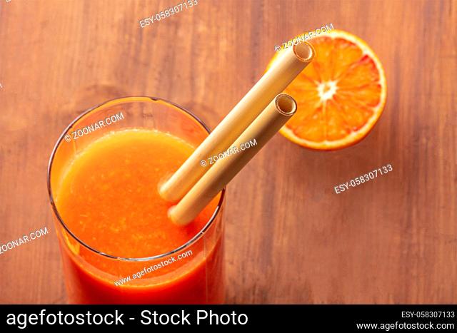 A closeup of reusable bamboo straws in a glass of vibrant orange juice. Selective focus
