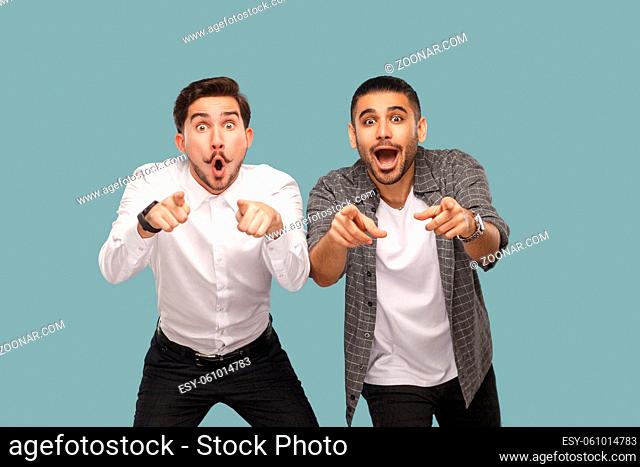 wow, are you serious? two surprised pointing finger handsome bearded friends standing and looking at camera with open mouth and big eyes